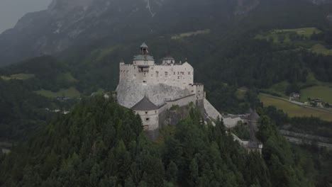 aerial orbit of medieval hohenwerfen fortress on top of a steep hill, surrounded by pine forest and berchtesgaden alps in werfen, salzburg, austria