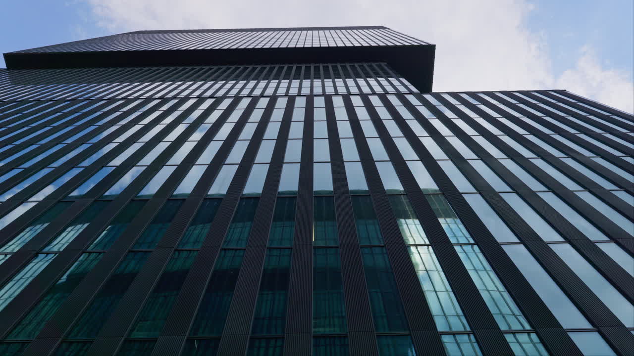 Low-angle trucking shot of skyscraper with the reflection of clouds among high buildings, business, and development concept