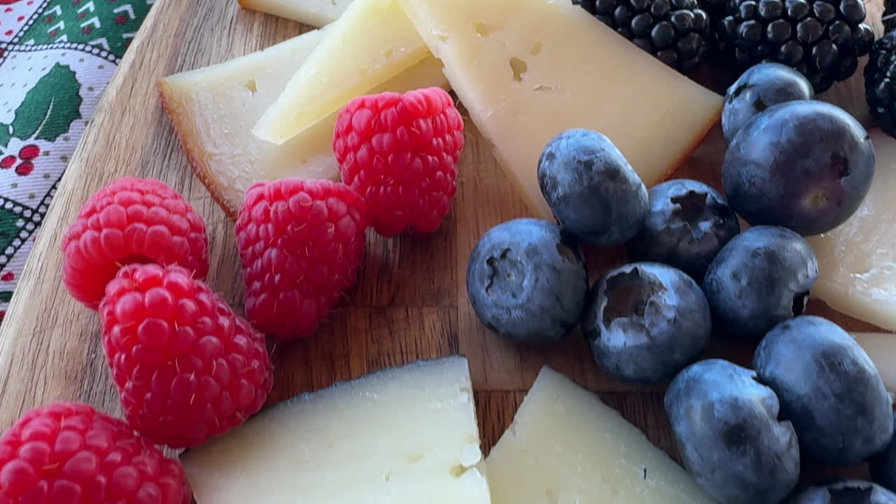 Close up of a wooden board with sliced cheese, raspberries, blueberries, and blackberries. Canarian cheese