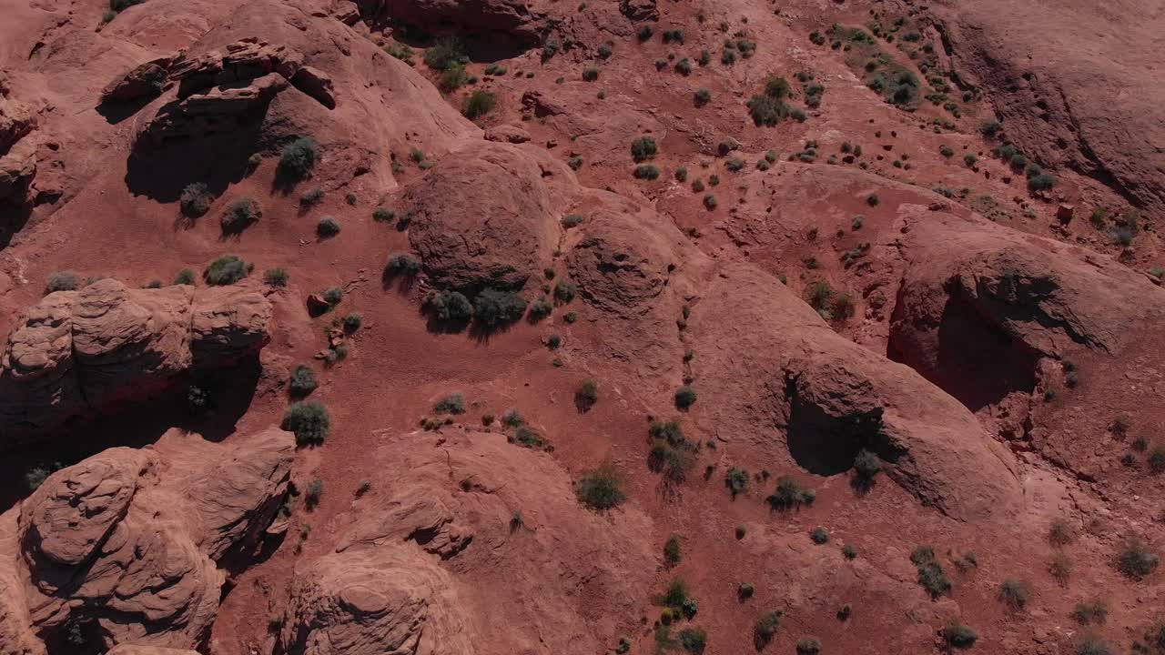 Drone che guarda in basso, poi esegue una panoramica lenta verso l'alto mentre avanza volando sopra una roccia rossa, osservando la città.