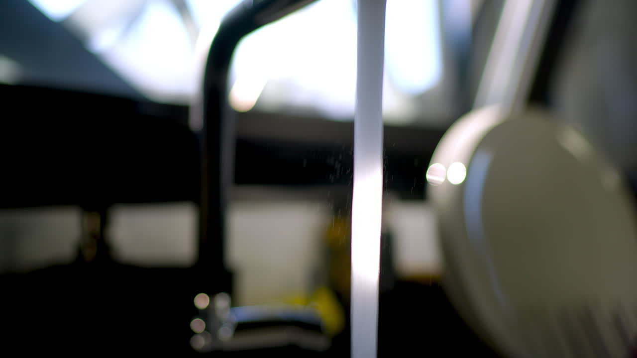 Clean, clear water streaming from sleek chrome faucet, natural light highlighting metallic surface and pure liquid flowing into kitchen sink with elegant simplicity