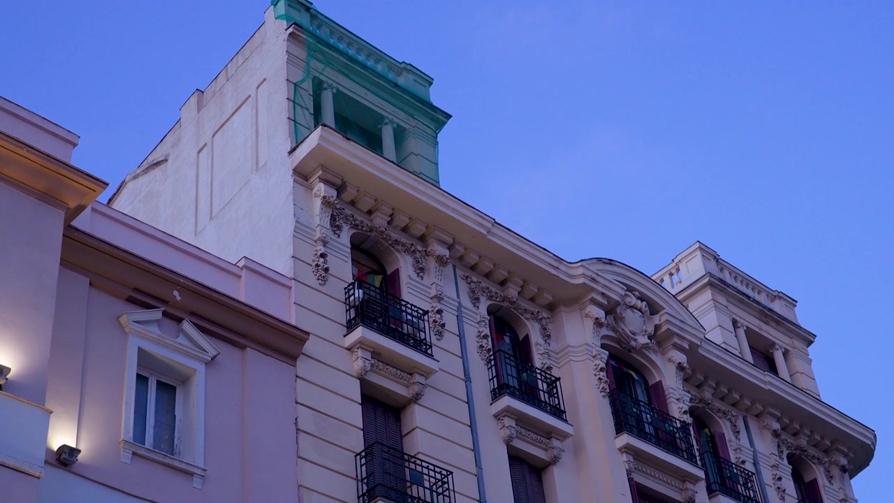 Toma en ángulo bajo de balcones ornamentados de edificios históricos y mampostería clásica en Madrid, España, durante la hora azul. Ideal para contenido de viajes y patrimonio urbano.