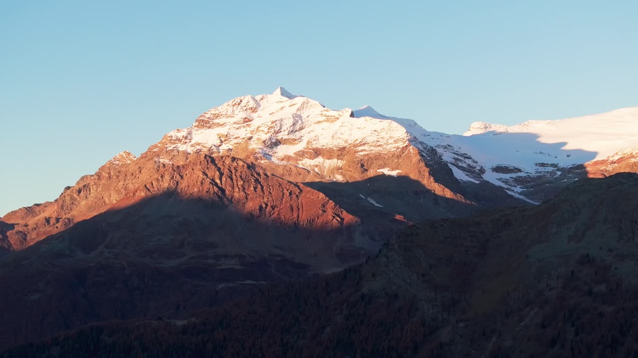 Aerial drone view of a mountain in autumn at sunrise. Colorful forest with snow on the mountain top