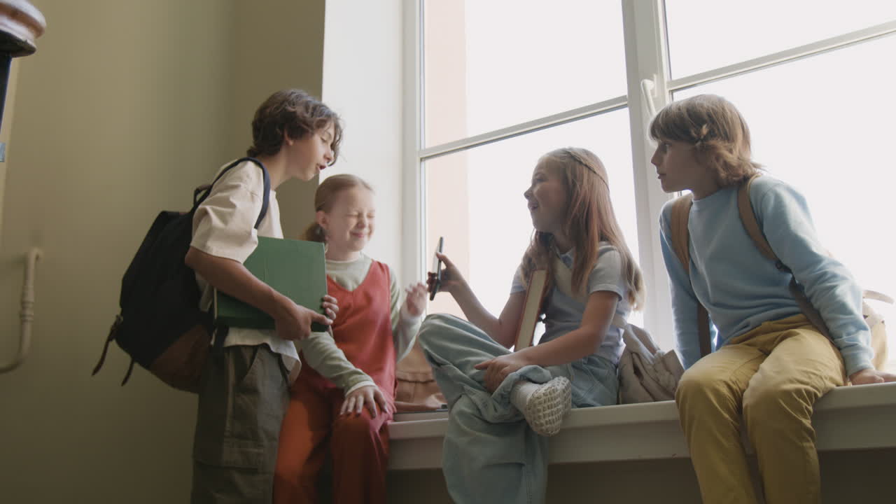Group of young students chatting and looking at a phone on a windowsill in school