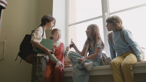 group of young students chatting and looking at a phone on a windowsill in school