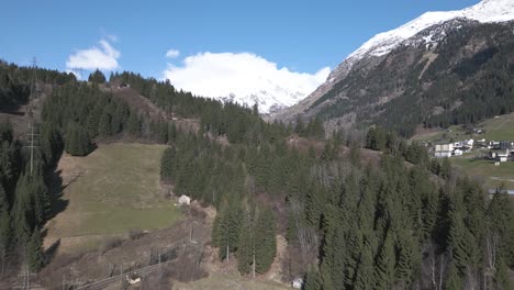 Vista-Aérea-Del-Soleado-Día-De-Primavera-En-Los-Alpes-Suizos,-Paisaje-Y-Pueblo-Bajo-Picos-Nevados