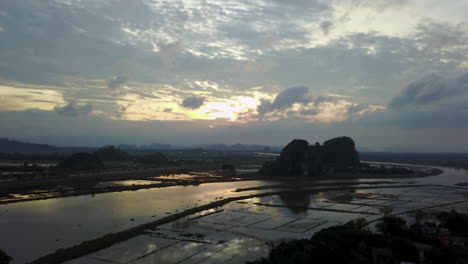 witness a breathtaking sunset in ninh binh, vietnam, with vibrant reflections painting the flooded rice fields and winding river beneath dramatic karst formations.