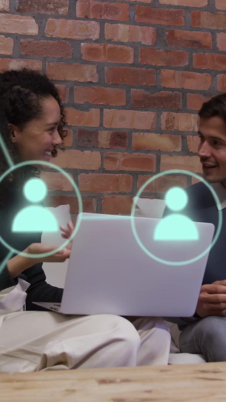 Vertical video: Woman typing on sofa, making nodes over laptop while man watching, picking tech