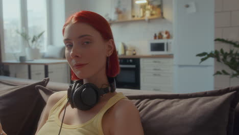 portrait of red-haired girl with headphones sitting on couch at home