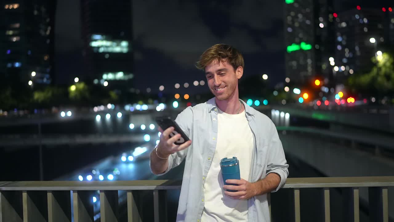 Man with phone and coffee cup on bridge at night