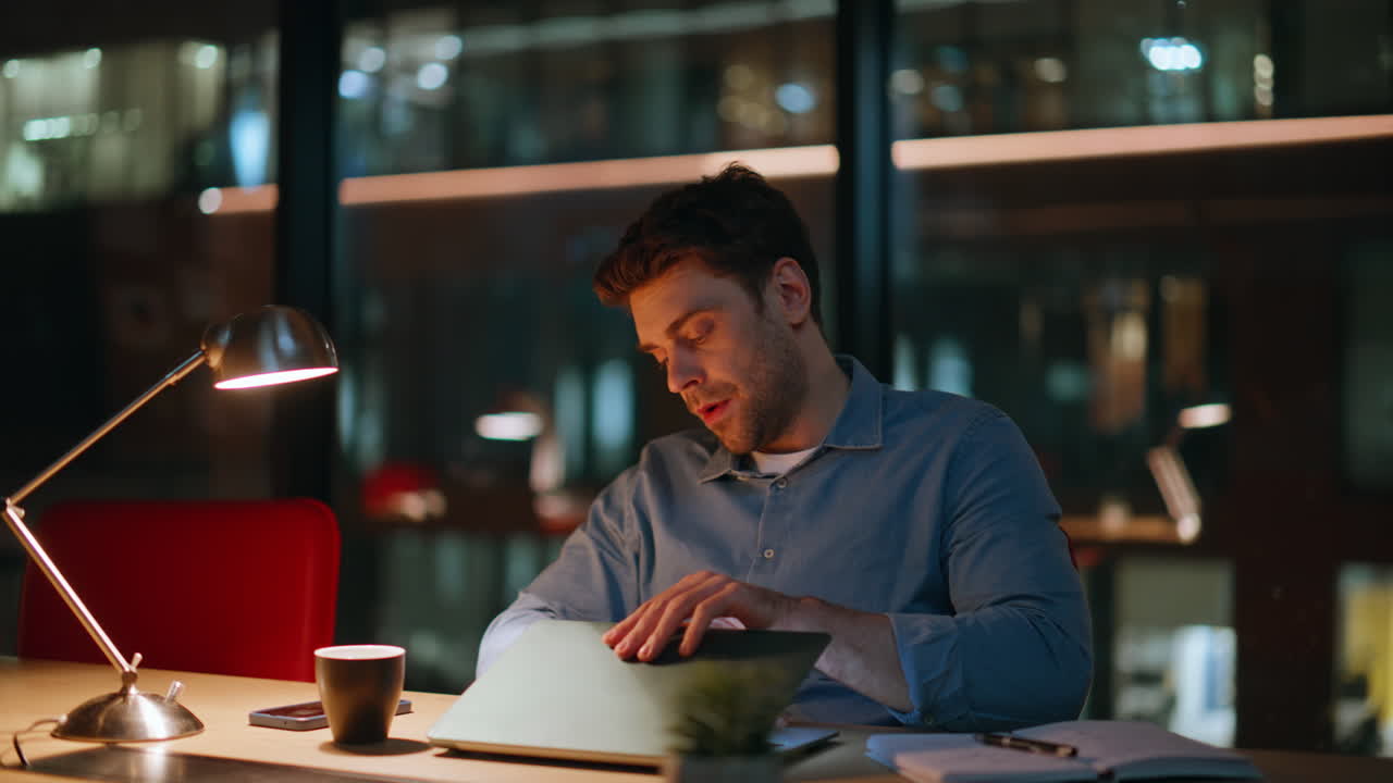 Primo piano di un lavoratore stanco che chiude il portatile in ufficio di notte, stufo degli straordinari