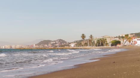 a very low angle shot of crushing in waves in slow motion with palm trees, houses and mountain hills in the background