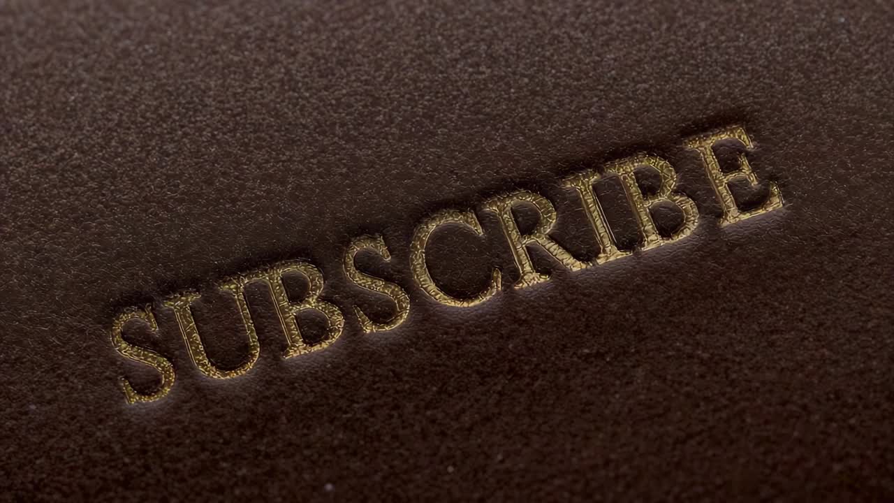 Moving camera revealing embossed SUBSCRIBE on brown leather in studio to show depth, gold rim
