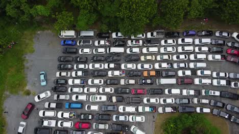 aerial: drone gaining altitude above a parking zone full by cars surrounded by jungle forest, stuck in the queue waiting for ferry from the koh chang island to mainland, thailand, asia