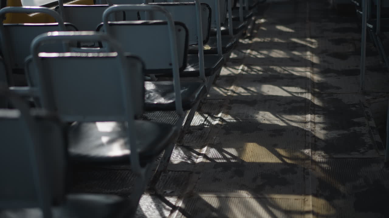 low view of empty bus seats as sun rays slice across aisle, long shadows ripple over worn floor, glints on metal frames and vinyl cushions, quiet midday ride mood with gentle motion