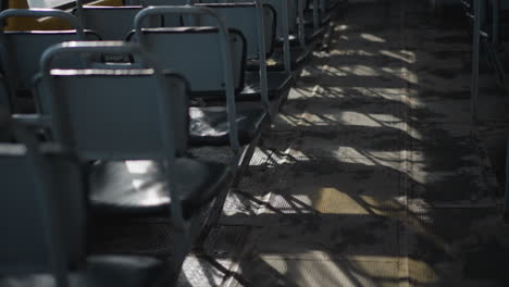 low view of empty bus seats as sun rays slice across aisle, long shadows ripple over worn floor, glints on metal frames and vinyl cushions, quiet midday ride mood with gentle motion
