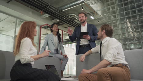 a business working group consisting of two women and two men have a relaxed meeting in the armchairs in the common area of the offices 4