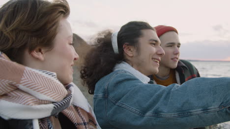 close up view of three teenage friends in winter clothes on seashore talking and looking the ocean on a windy day