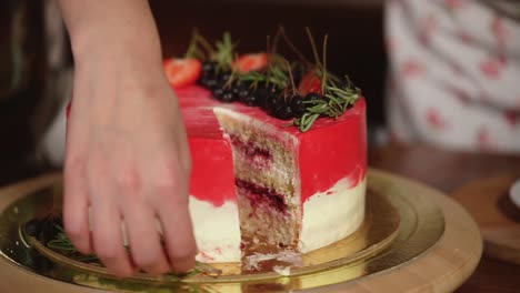 a hand cutting a beautifully decorated red and white cake with fresh berries and herbs.