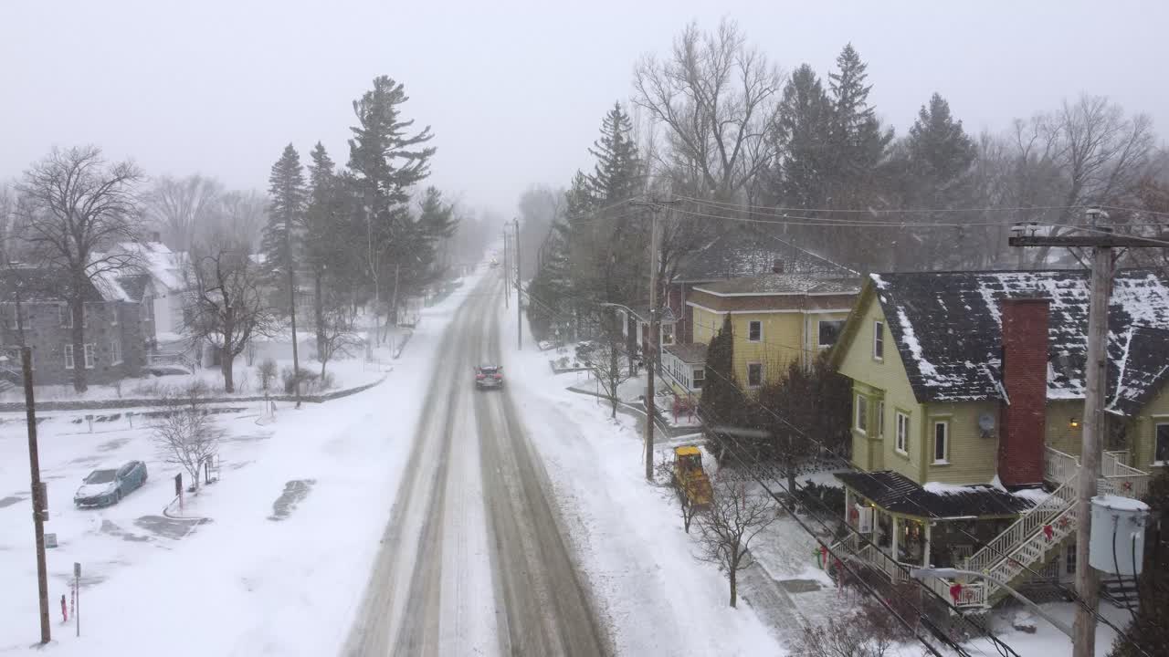Drone dolly over a snowy neighborhood as a snow plow clears sidewalks and cars drive