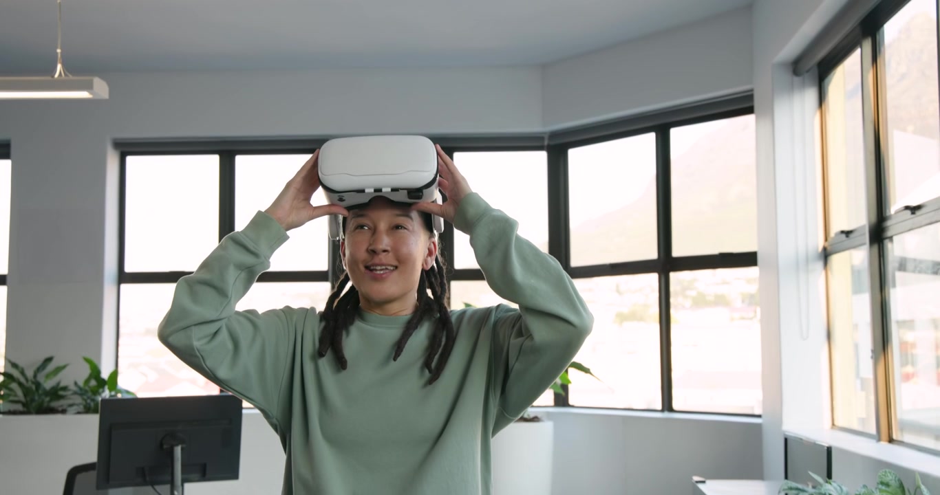 Persona africana non binaria con una maglia verde che indossa un visore VR bianco, esplorando una scena in un ufficio con una pianta.