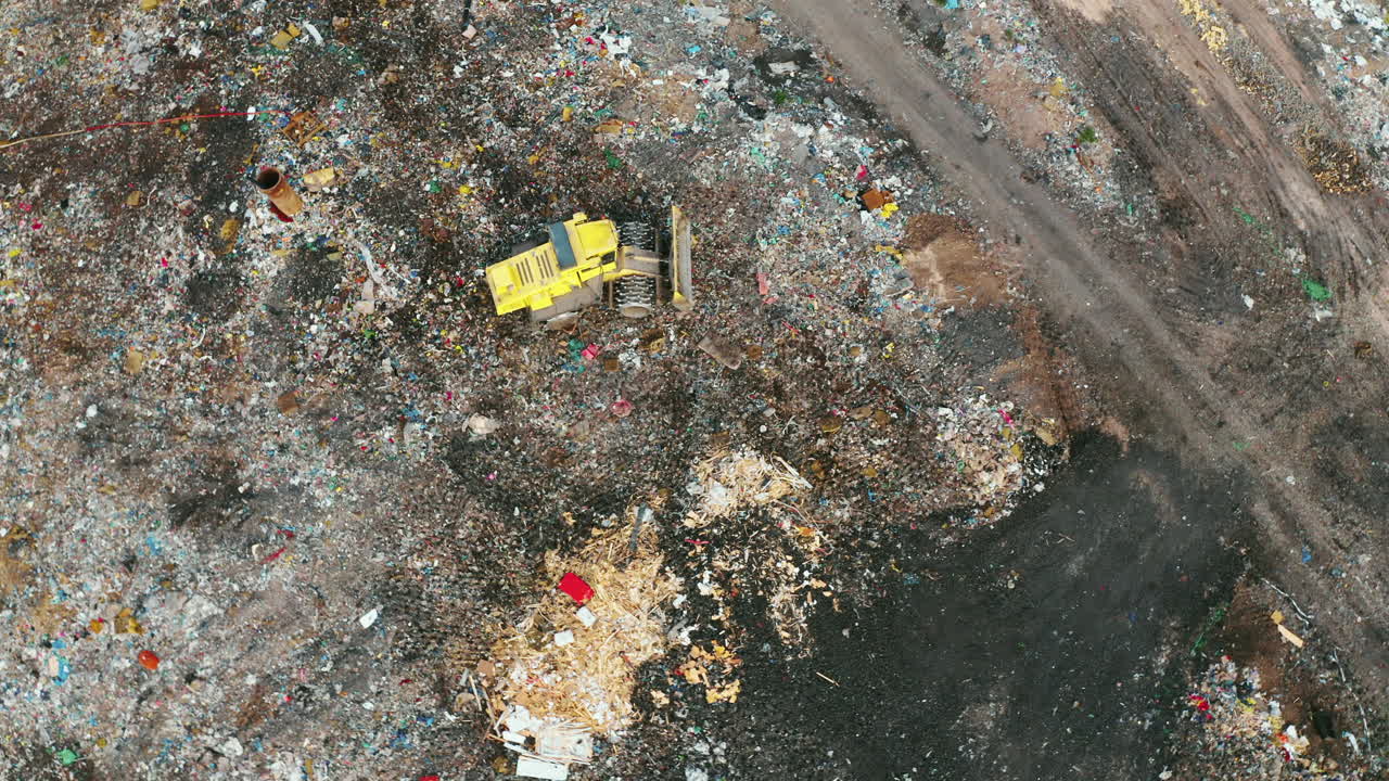 High-quality footage of landfill with geomembrane, drone cruising over garbage trucks and tractors operating, birds flying above trash, nature surrounding energy plant
