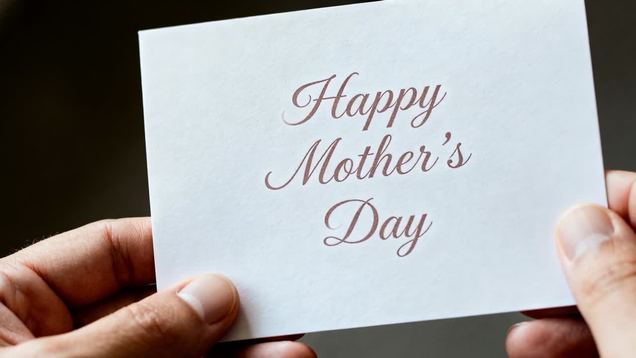 Hands bringing white card into frame, centering cursive 'Happy Mother's Day' for card designers