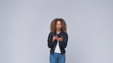 Foto-De-Estudio-De-Una-Mujer-Con-Chaqueta-De-Cuero-Enviando-Mensajes-De-Texto-Por-Teléfono-Móvil-En-Cámara-Lenta