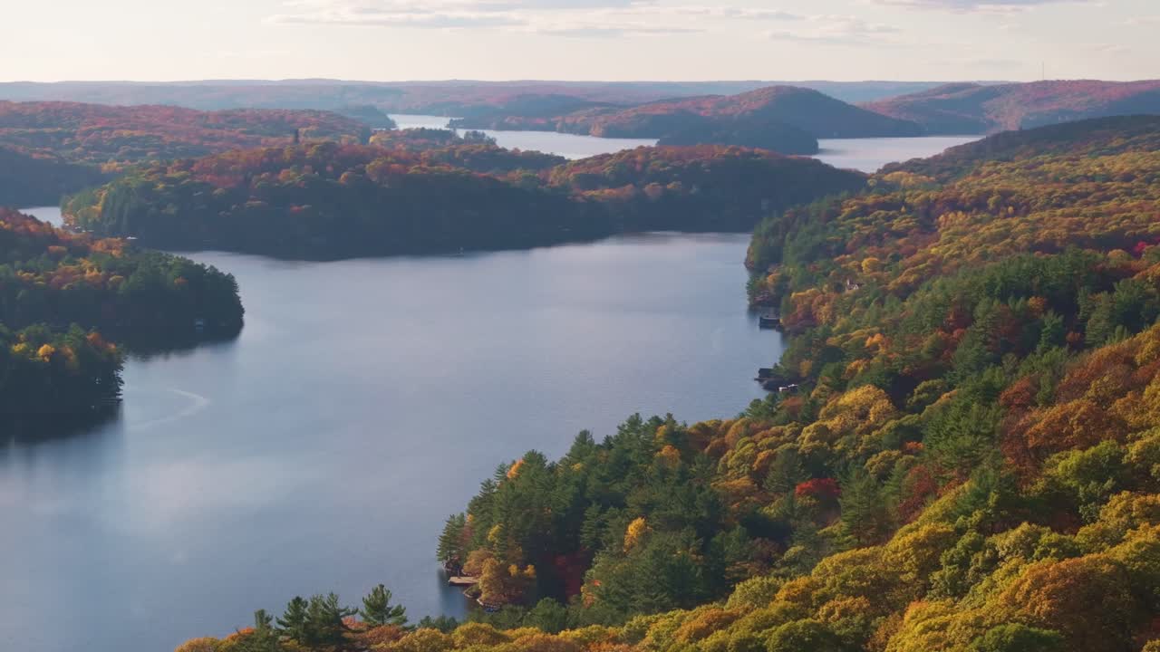 A serene lake surrounded by vibrant autumn forest with rolling hills, aerial view