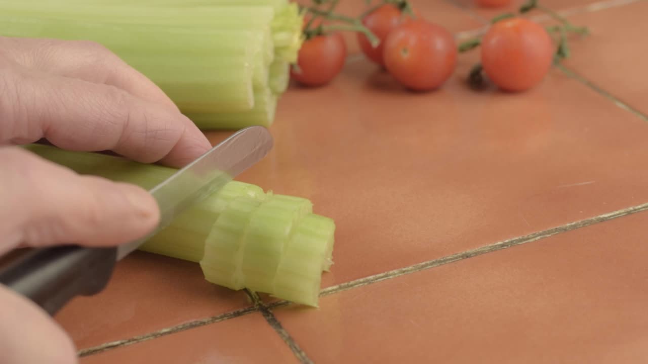 Slicing celery sticks with knife in kitchen medium shot