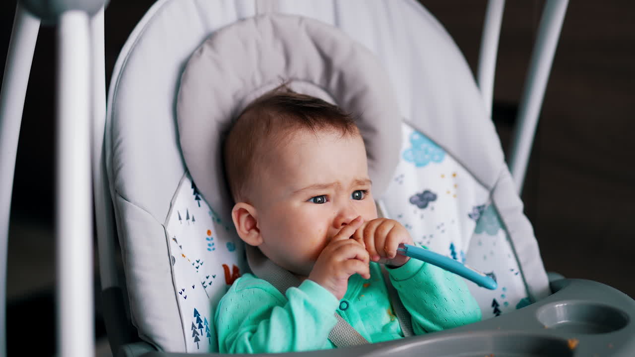 Cute boy with splotchy face holds a spoon. Kid shows the spoon into mouth and makes a grimace.