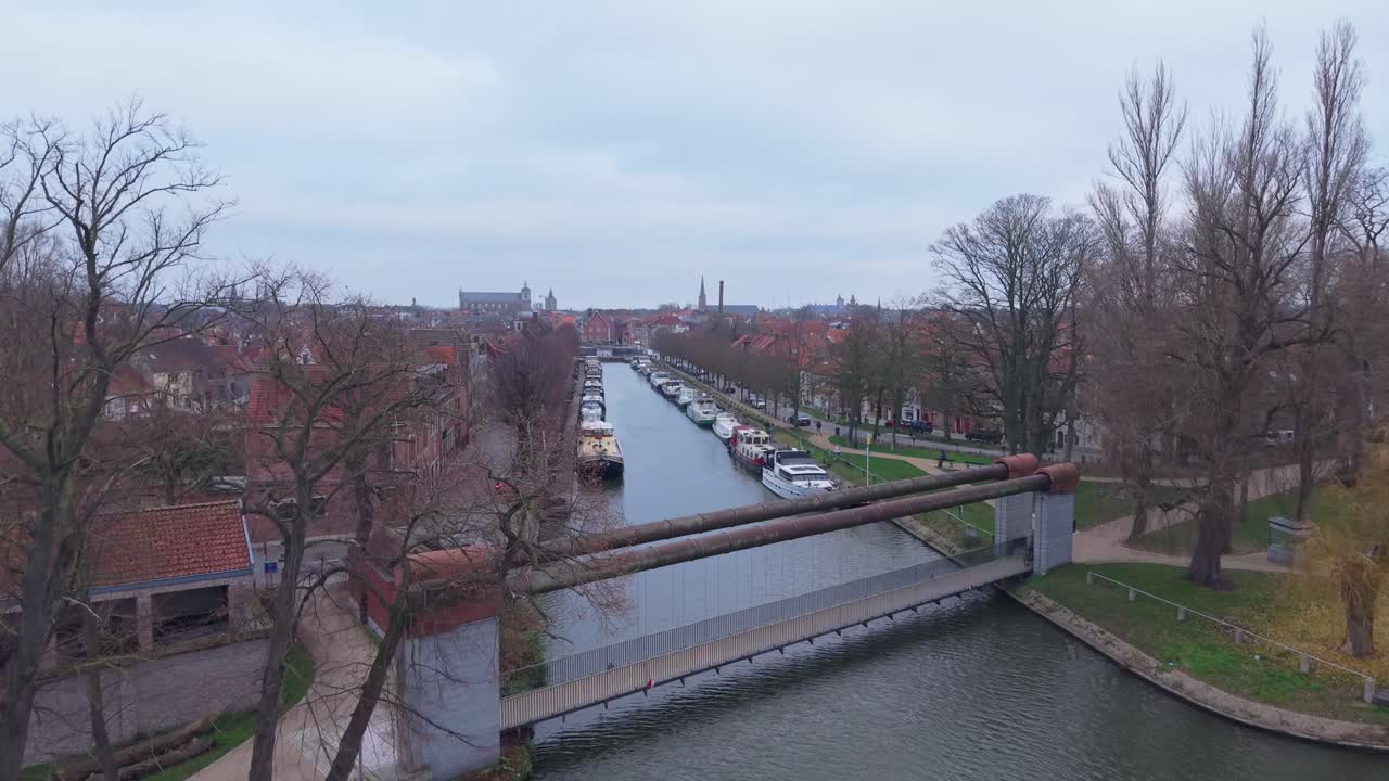 Lávka v Bruggách s projíždějícím kolem, odhalující historické panorama města, kanály a okouzlující architekturu