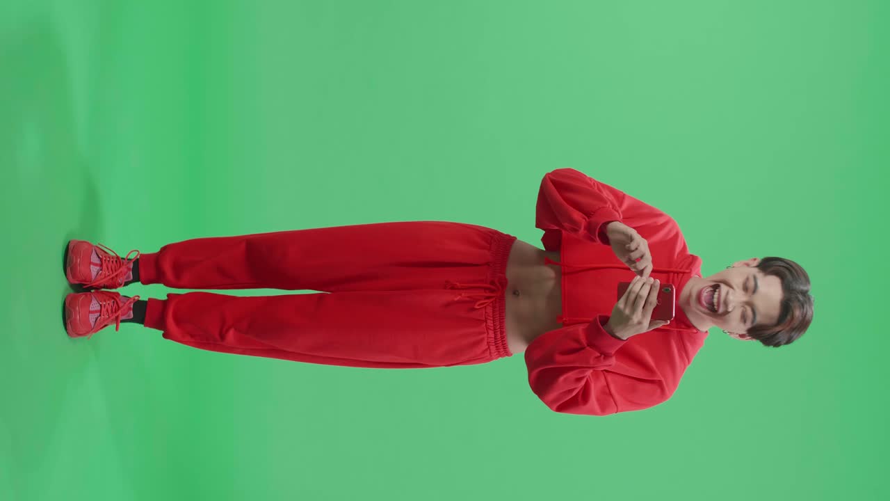 Full Body Of Happy Asian Transgender Male Enjoy Using Mobile Phone While Standing On Green Screen In The Studio