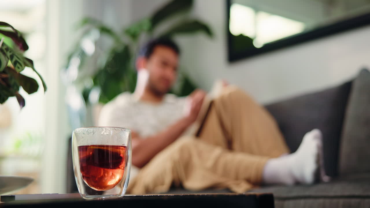 背景にソファで本を読む男性がいるホットティーのグラス。