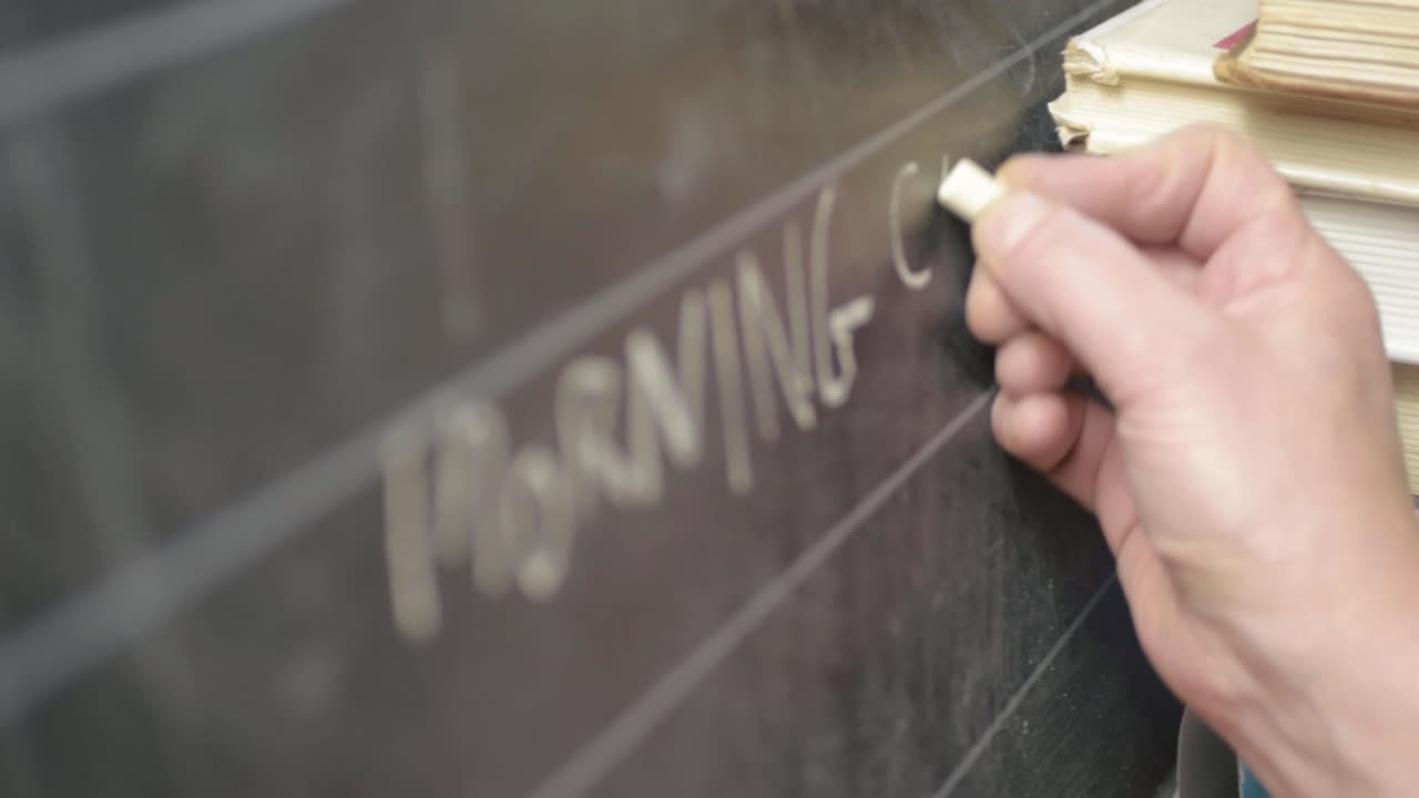 Hand writing on blackboard with chalk panning shot