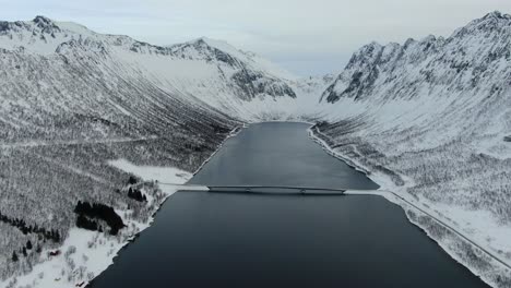 vista de drones en el área de tromso en invierno volando sobre un fiordo rodeado de montañas blancas y un puente que cruza en noruega