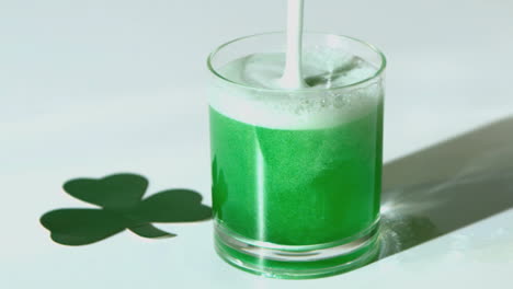 cerveza verde vertiendo en el vaso al lado del trébol de papel