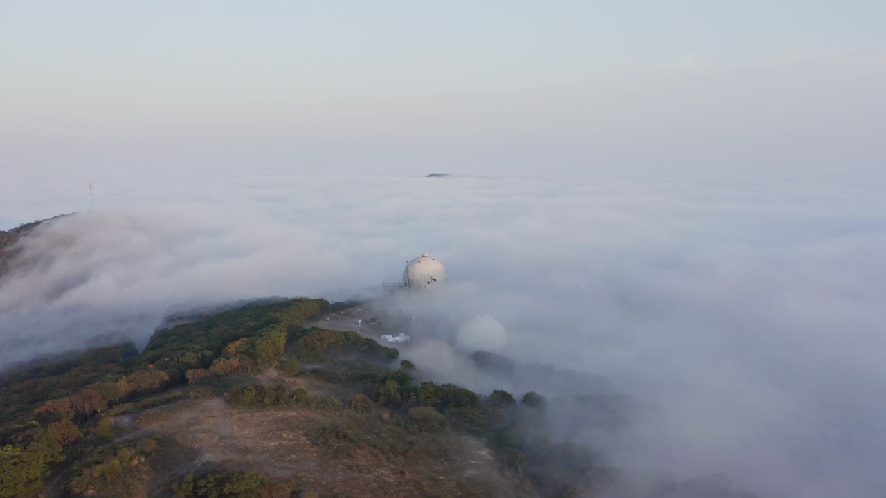 저녁에 여러 구조물이 있는 언덕을 덮고 있는 짙은 안개 구름