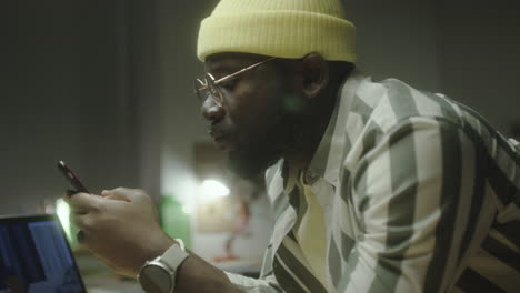 a man in a yellow beanie and glasses using his smartphone