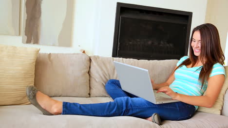 una bonita morena relajándose en el sofá usando una computadora portátil