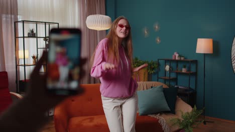 blogger adolescente alegre bailando en la cámara filmando video usando el teléfono móvil en casa en la sala de estar