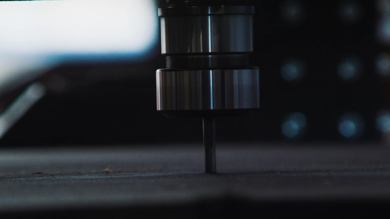 Timelapse di una testa CNC, primo piano frontale minimale di una punta CNC sospesa appena sopra la superficie piana di una tavola