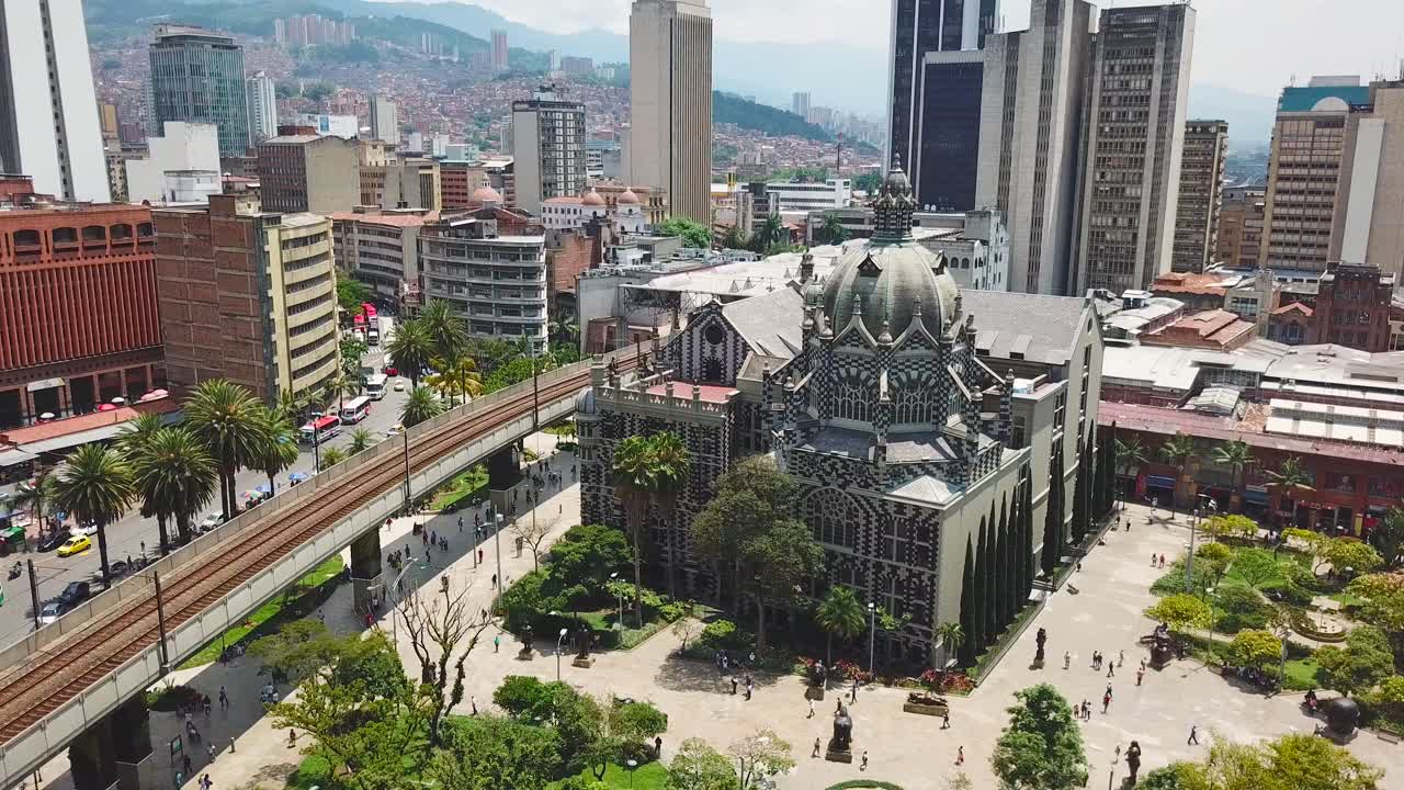 Imagens de drone estáticas mostrando igreja e metrô na Praça Botero, com sol forte na praça de Medellín.