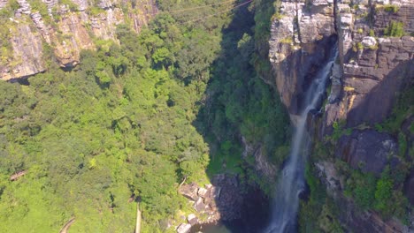 una alta cascada en cascada en un cañón verde exuberante rodeado de denso bosque, vista aérea