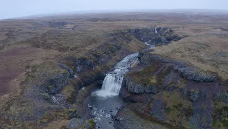 Toma-De-órbita-Aérea-Que-Muestra-Una-Cascada-Cayendo-En-El-Río-Sela-Durante-Las-Nubes-En-El-Cielo-En-Escandinavo