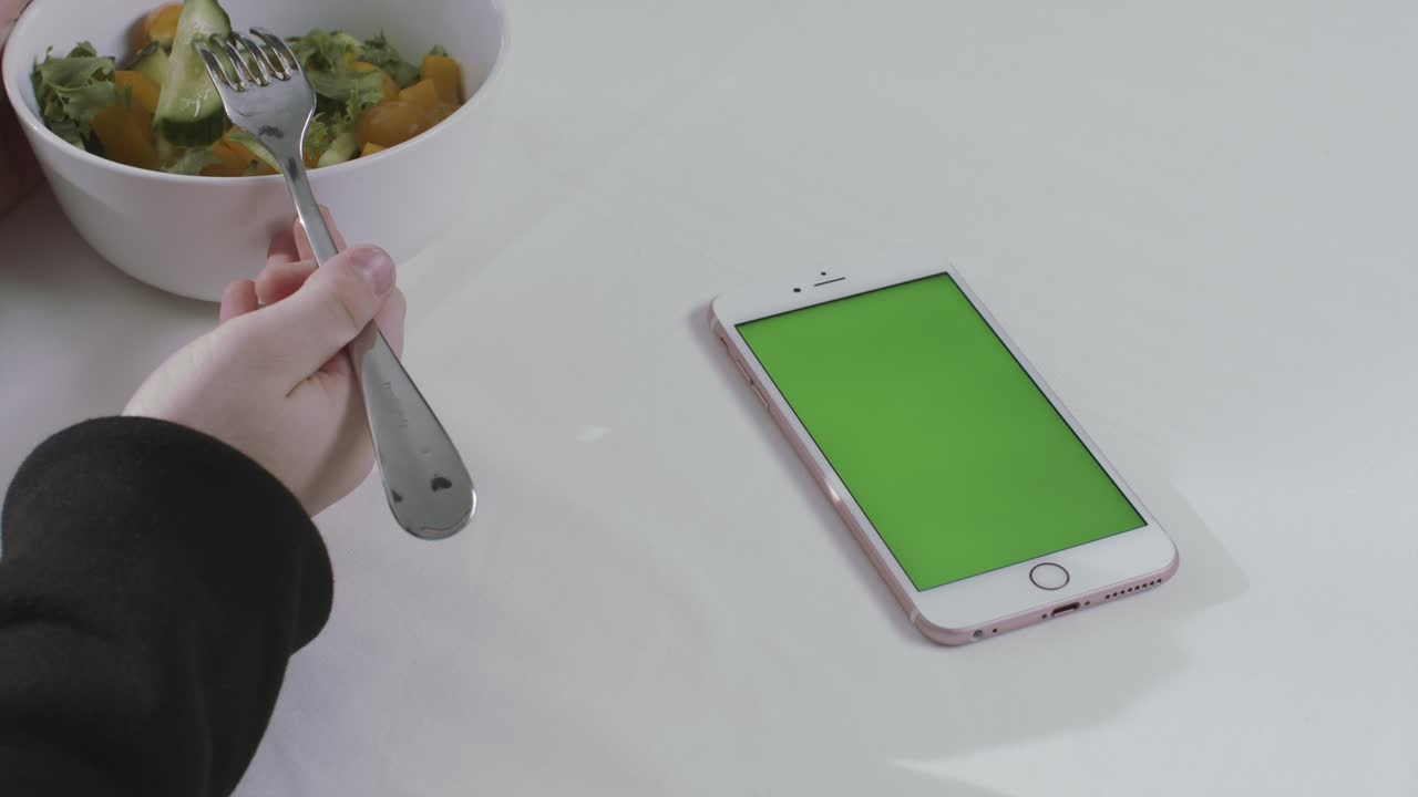 persona comiendo ensalada mientras usa un teléfono con una pantalla verde