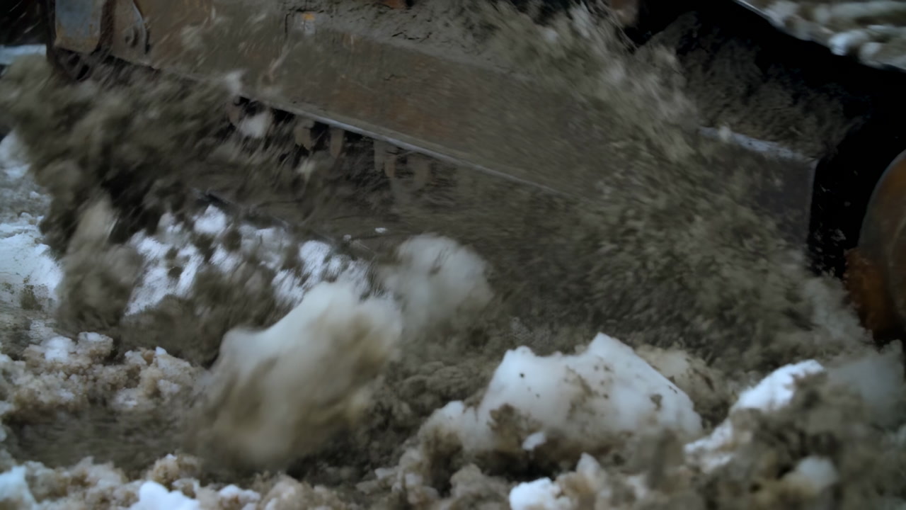 Tracked Bulldozer Treads Crushing Icy Slush And Mud, Flinging Dirty Snow Across Rusted Undercarriage