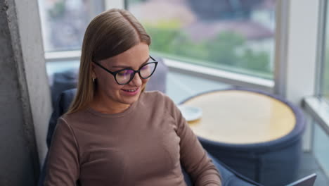 smiling relaxed blonde lady typing on her laptop. work in comfortable modern office atmosphere. high angle view.