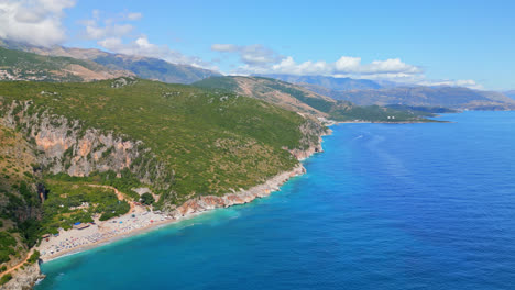 aerial drone high angle shot over tourists thronging along the secluded gjipe beach, albania on a sunny day