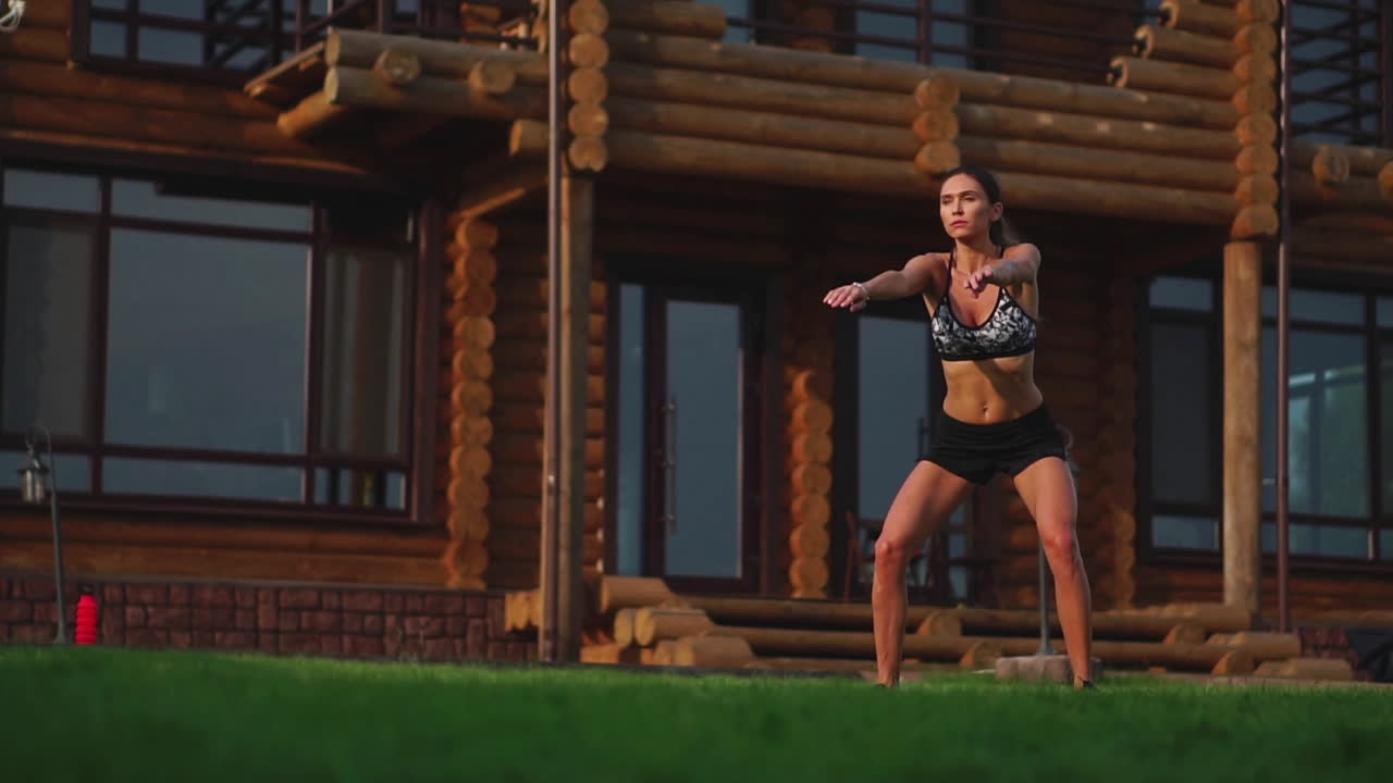 큰 저택의 배경에 아름다운 갈색, 체육관에 종사하고 squats를 수행, 야외에서 운동